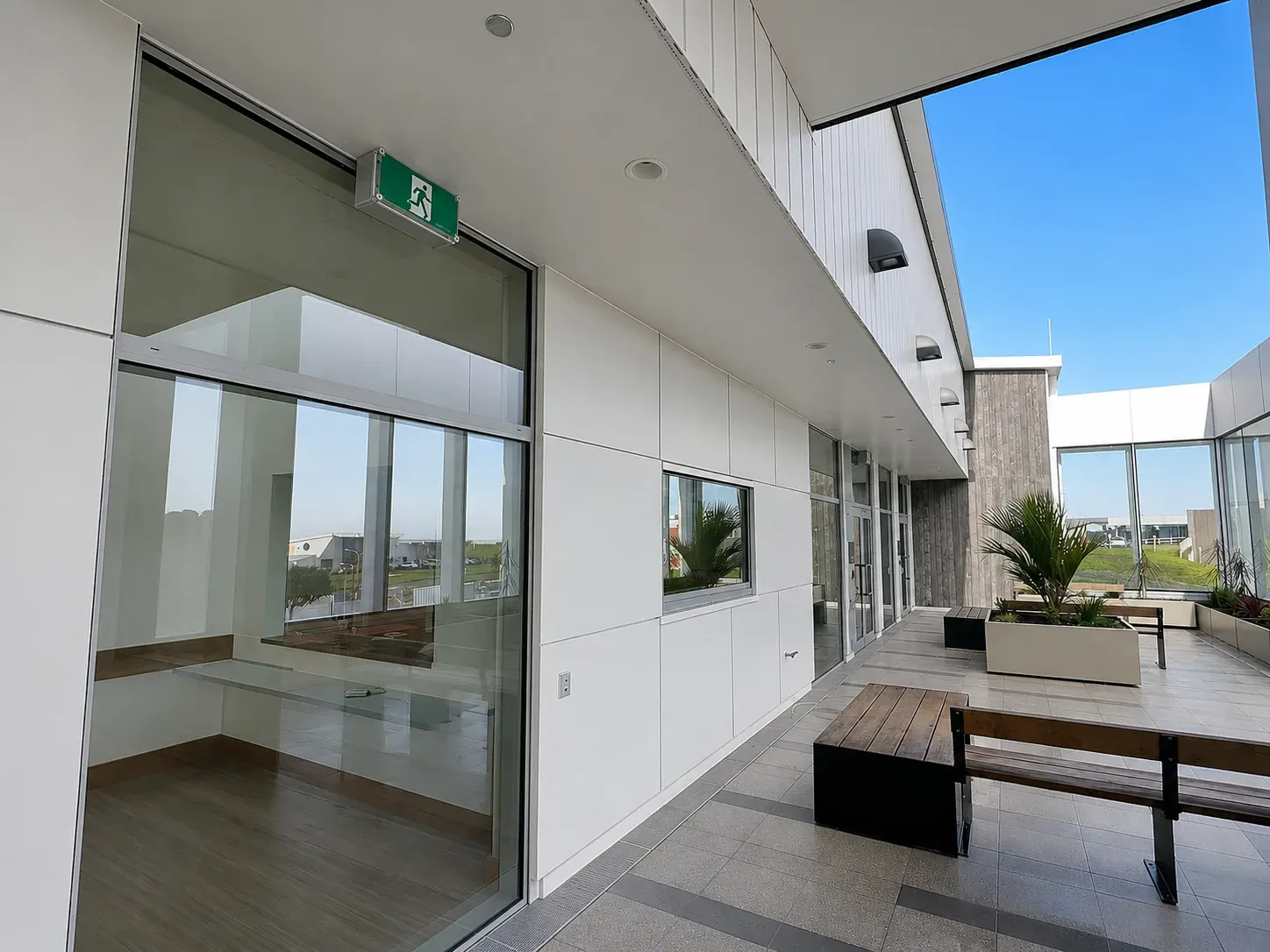 A sheltered courtyard at the West Coast mental health facility, white cladding and full-height glazing around a planted seating area