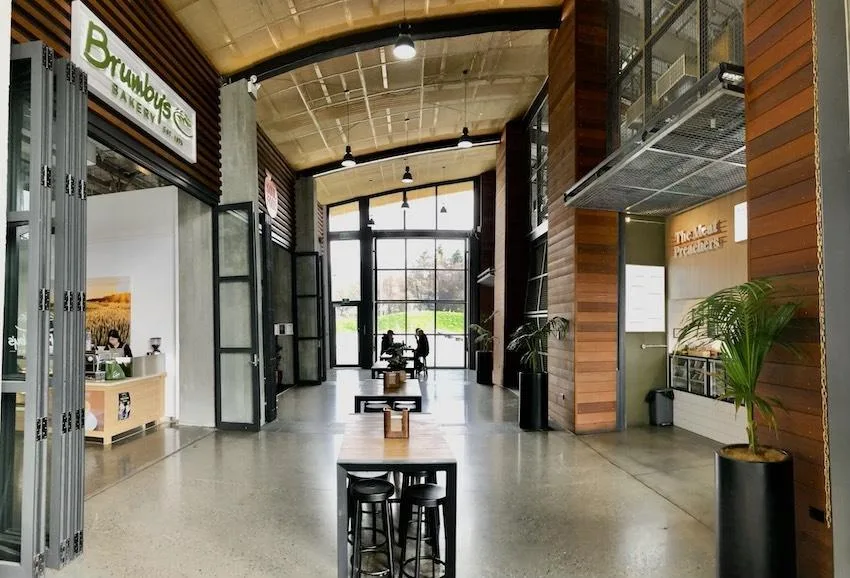 The interior mall at Queenstown Central, a bakery and food tenancies either side of a polished concrete walkway under a curved timber ceiling