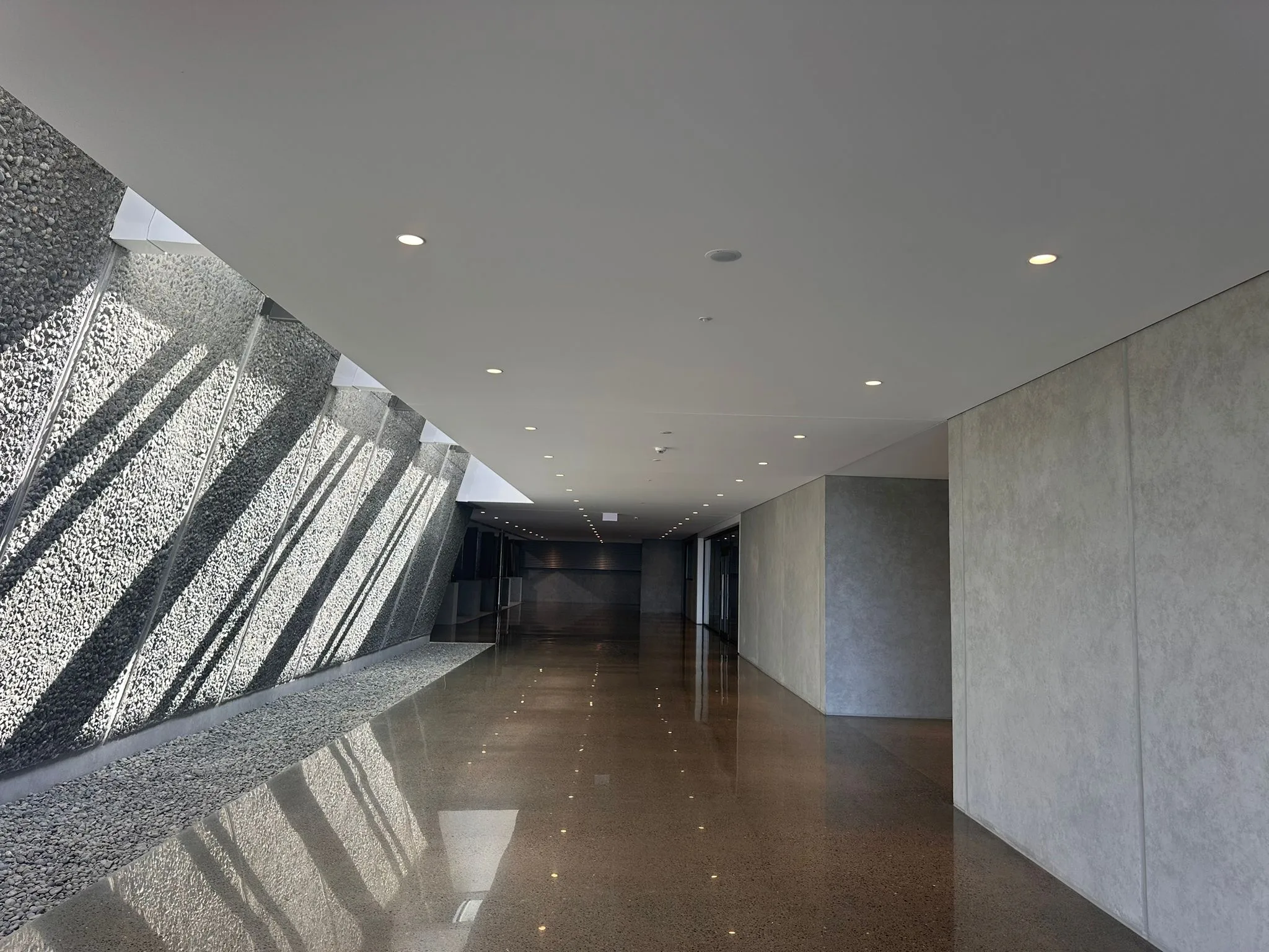 A further view of the Delegat Winery circulation space, daylight raking down the aggregate wall onto the polished floor