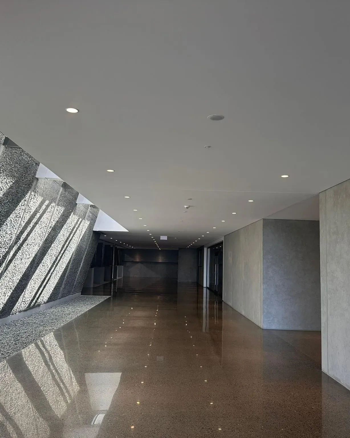 An interior circulation space at Delegat Winery, pale walls and ceiling above a polished concrete floor, with an angled aggregate wall to one side