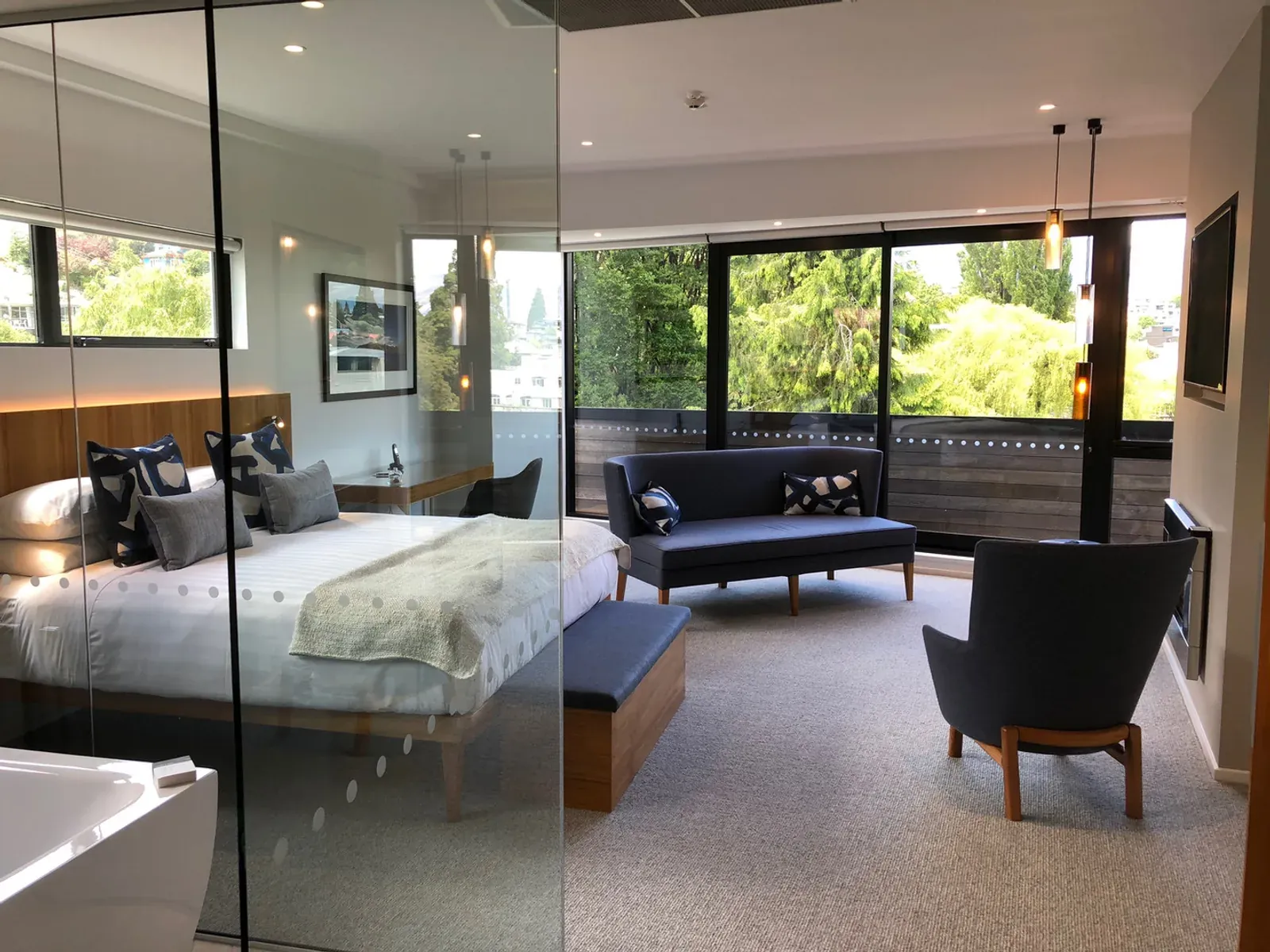 A guest suite at Queenstown Park Boutique Hotel, glazed bedroom partition beside a seating area opening to trees through full-height windows
