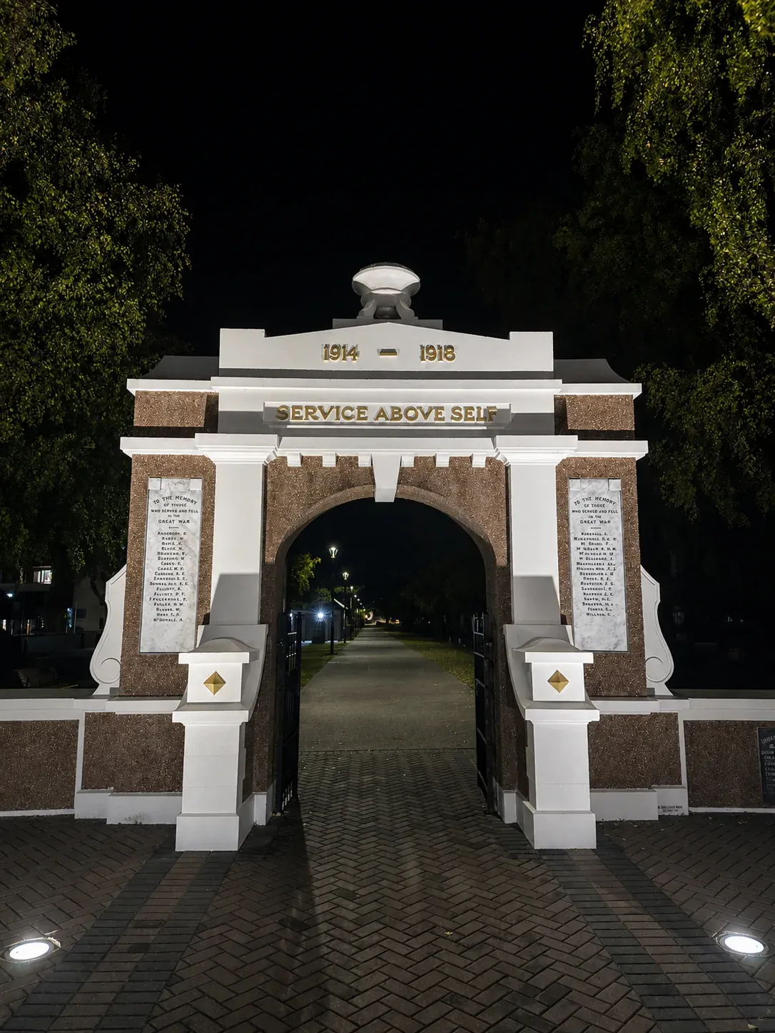 The memorial archway lit at night, cream plaster against the dark, with the memorial name panels either side