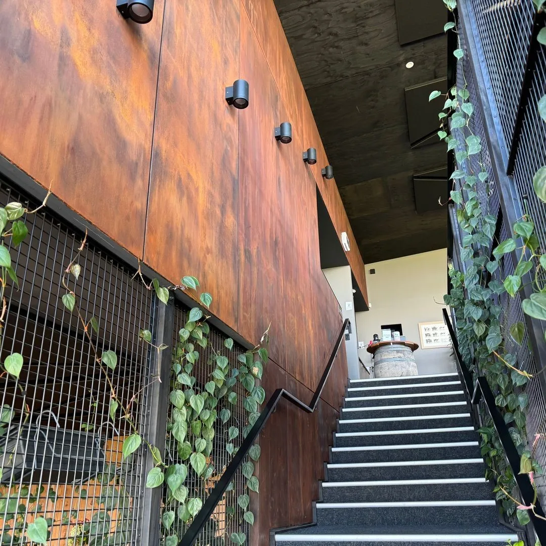 The rust-effect finish on the stairwell wall at The Fancy Cow, trailing plants spilling over the black mesh balustrade alongside