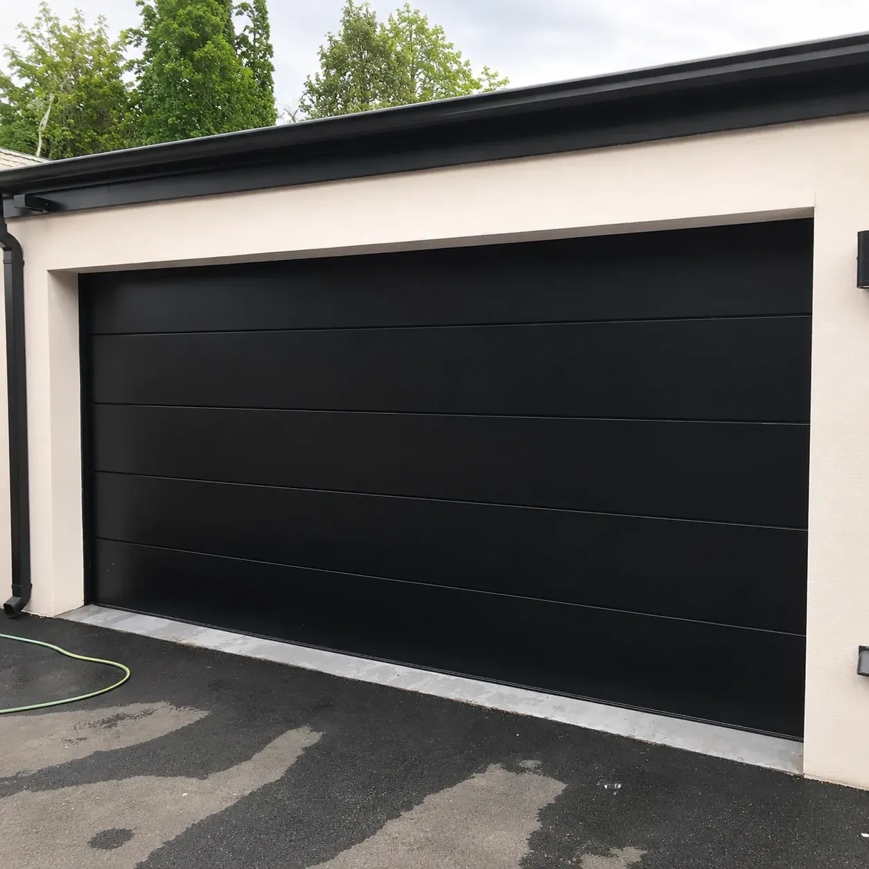 A garage door and surround finished in deep black AluLuxe coating against a pale plaster wall