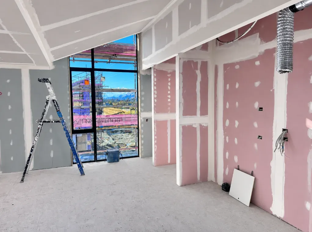 Interior plastering in progress, stopped and sanded plasterboard walls in a new build with the framing and glazing beyond