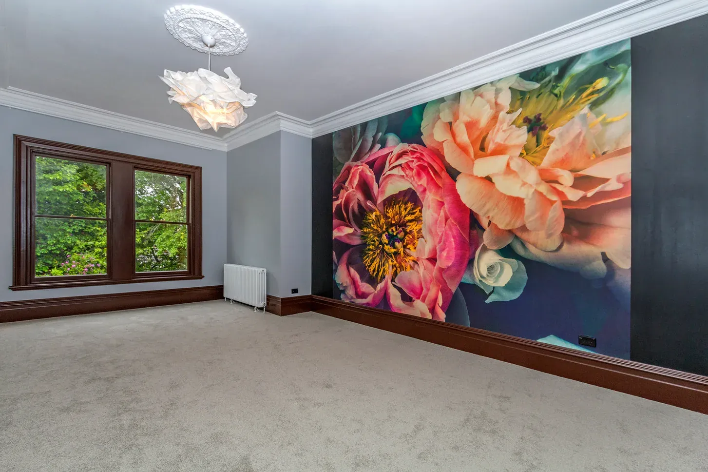 A floral mural wallpaper covering a feature wall in a heritage room, with a ceiling rose, timber sash window, and pale carpet