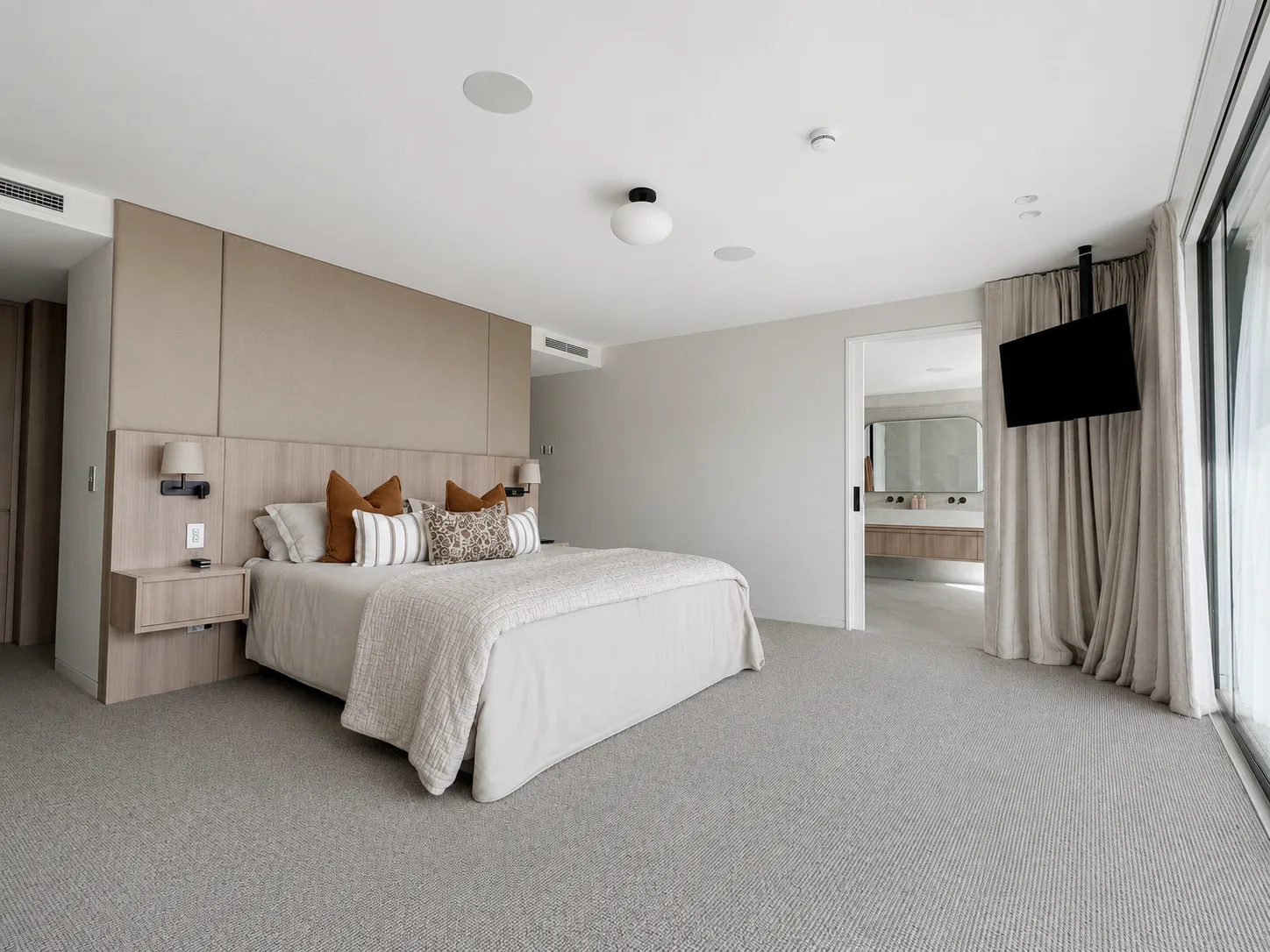 A bedroom at Little Akaloa, neutral walls and an upholstered headboard wall, opening through to an ensuite