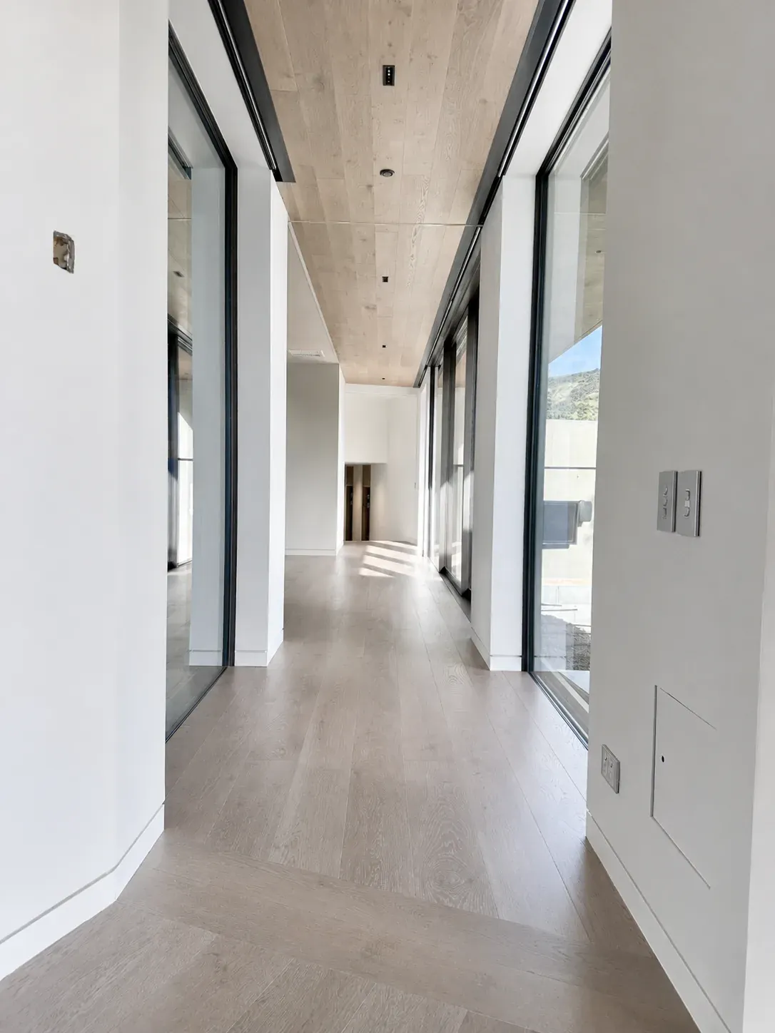 A hallway at Little Akaloa, white walls under a timber-lined ceiling, with full-height glazing to the hillside