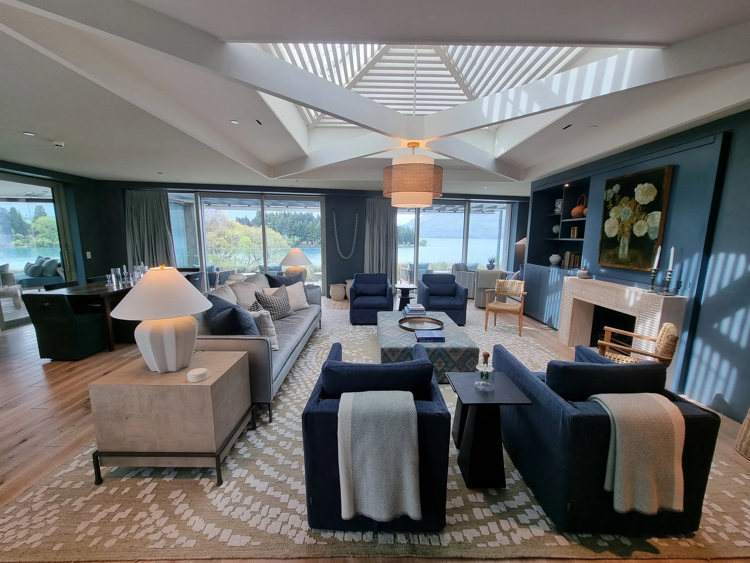 A Roki Collection penthouse lounge, cream ceiling above deep blue walls, opening to Lake Wakatipu and the mountains beyond