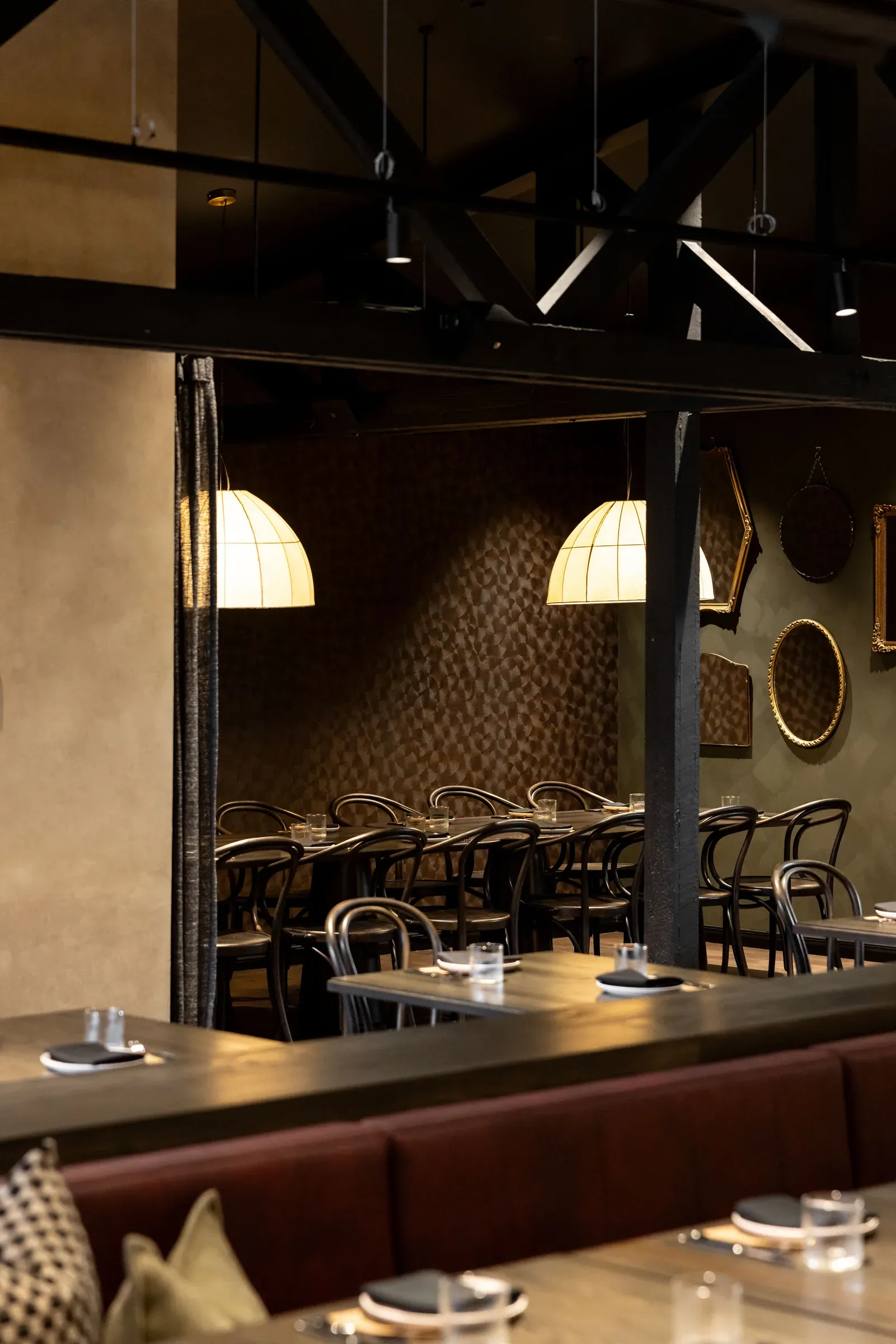 The private dining room at Toast and Oak, its impasto feature wall lit by two shaded pendants and hung with gilt mirrors, seen past the main dining tables